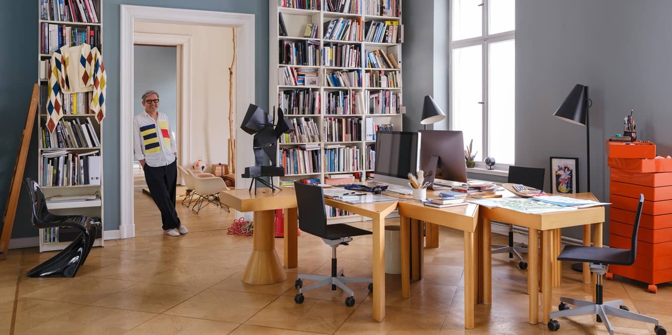 Arbeitszimmer in einer Berliner Altbauwohnung mit hohen B&uuml;cherregalen, Holztischen und einem Mann im T&uuml;rrahmen